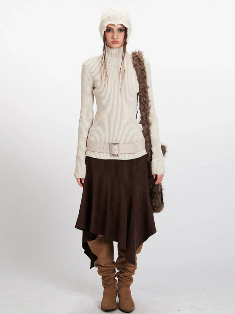 Woman wearing a cream ribbed knit turtleneck sweater, brown asymmetrical hem skirt, cream knit beanie, and brown suede boots.