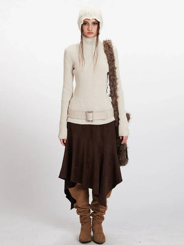 Woman wearing a cream ribbed knit turtleneck sweater, brown asymmetrical hem skirt, cream knit beanie, and brown suede boots.