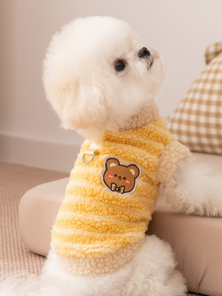Side view of a small white dog in a yellow striped fleece vest with a bear applique