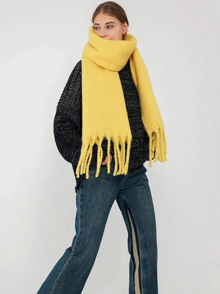 Full body shot of a woman wearing a bright yellow scarf with fringes, demonstrating its size and drape.
