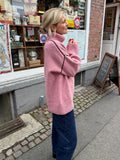 Woman wearing a pink oversized turtleneck knit sweater with contrasting black seams