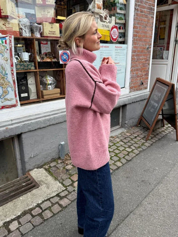 Woman wearing a pink oversized turtleneck knit sweater with contrasting black seams