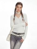 Woman posing with arms crossed wearing a white long-sleeve top and grey jeans.