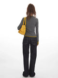 Back view of a woman wearing a grey long-sleeve Henley top with contrast green cuffs and hem, and dark wash baggy jeans