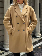 Woman wearing a camel double-breasted coat with hands in pockets.
