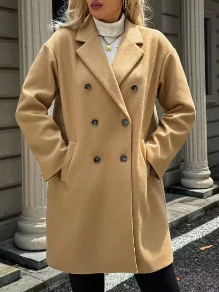 Woman wearing a camel double-breasted coat with hands in pockets.