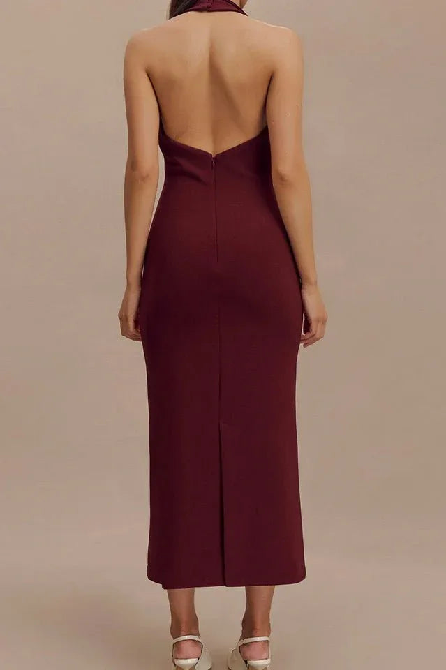 Back view of a woman in a burgundy sleeveless midi sheath dress with a deep V-neck, sharp collar, and open back.