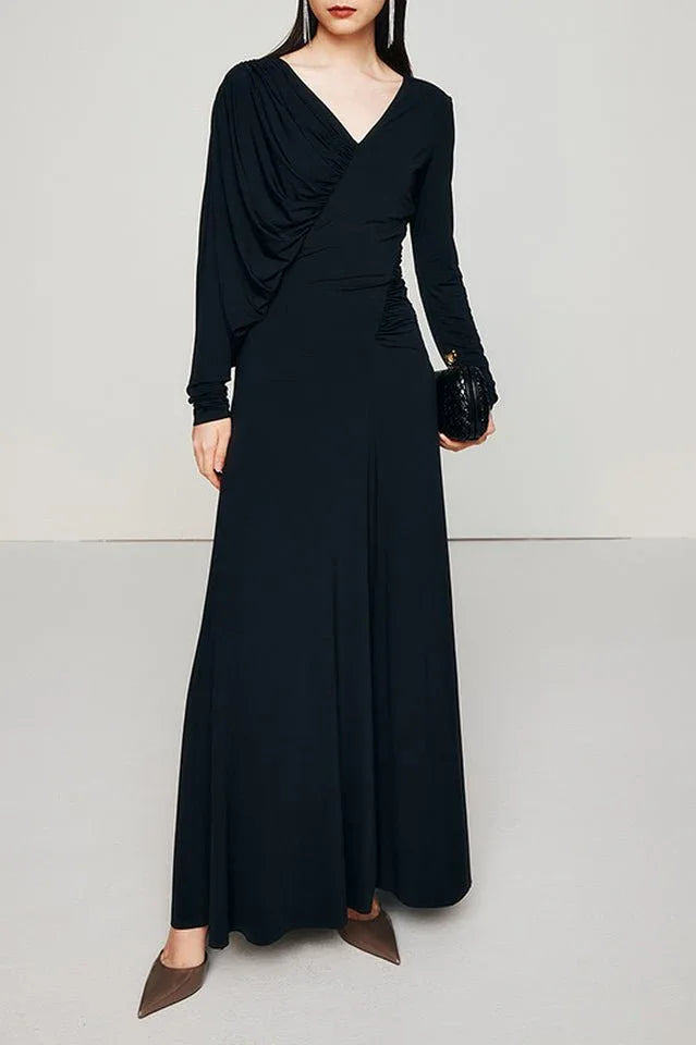 Woman wearing a long black ruched V-neck dress with long sleeves.