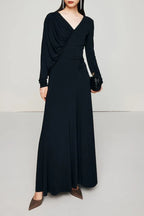 Woman wearing a long black ruched V-neck dress with long sleeves.
