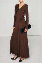 Woman wearing a long brown ruched V-neck dress with long sleeves and holding a black clutch.