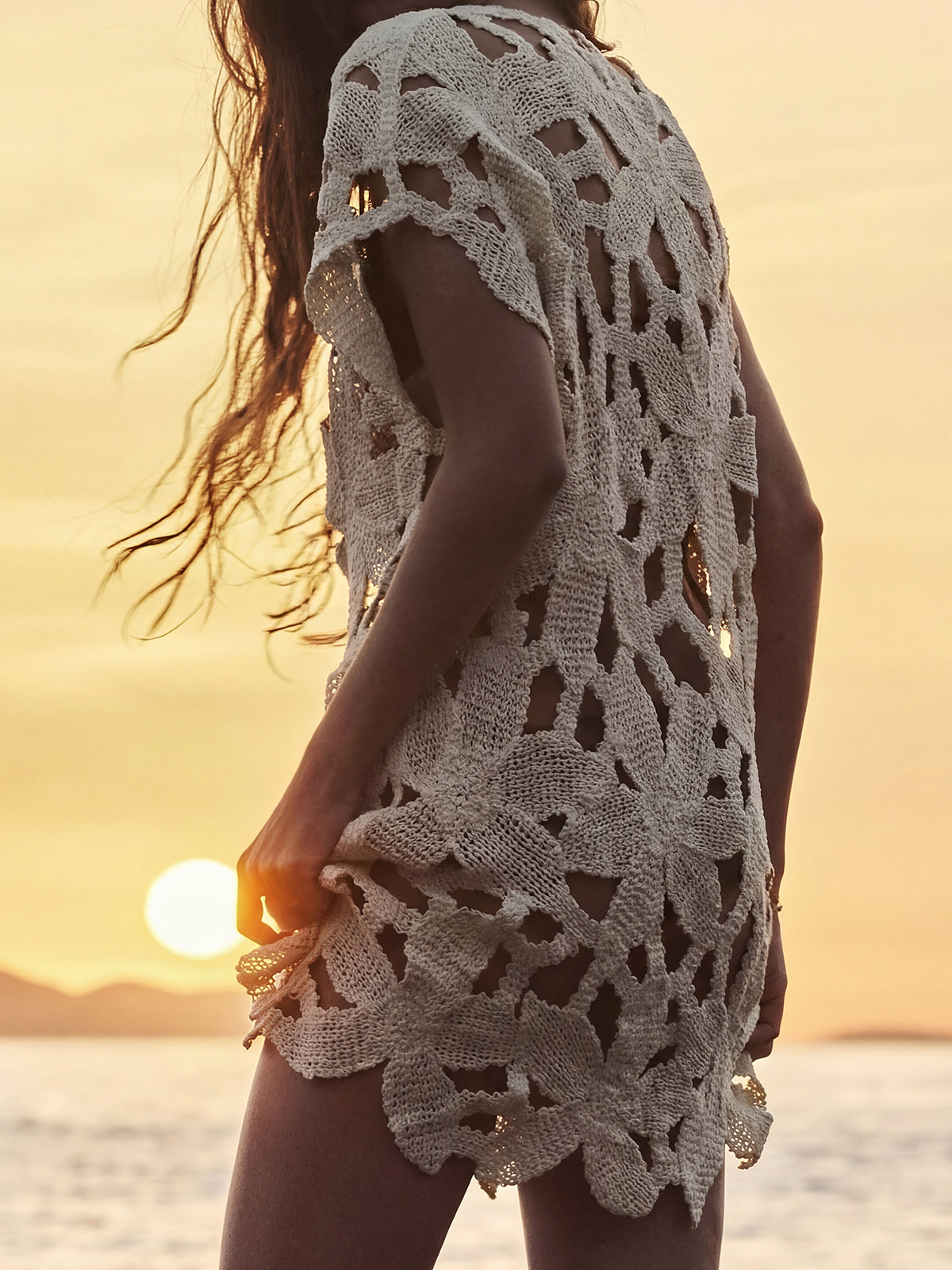 Back view of a woman in a cream openwork knit tunic at sunset