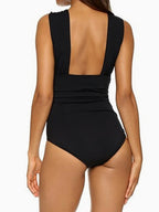 Back view of a woman wearing a black one-piece swimsuit with a plunging back neckline and ruched waist detail