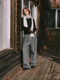 Full body shot of a woman in a cream scarf, black sweater, and grey wide-leg pants.