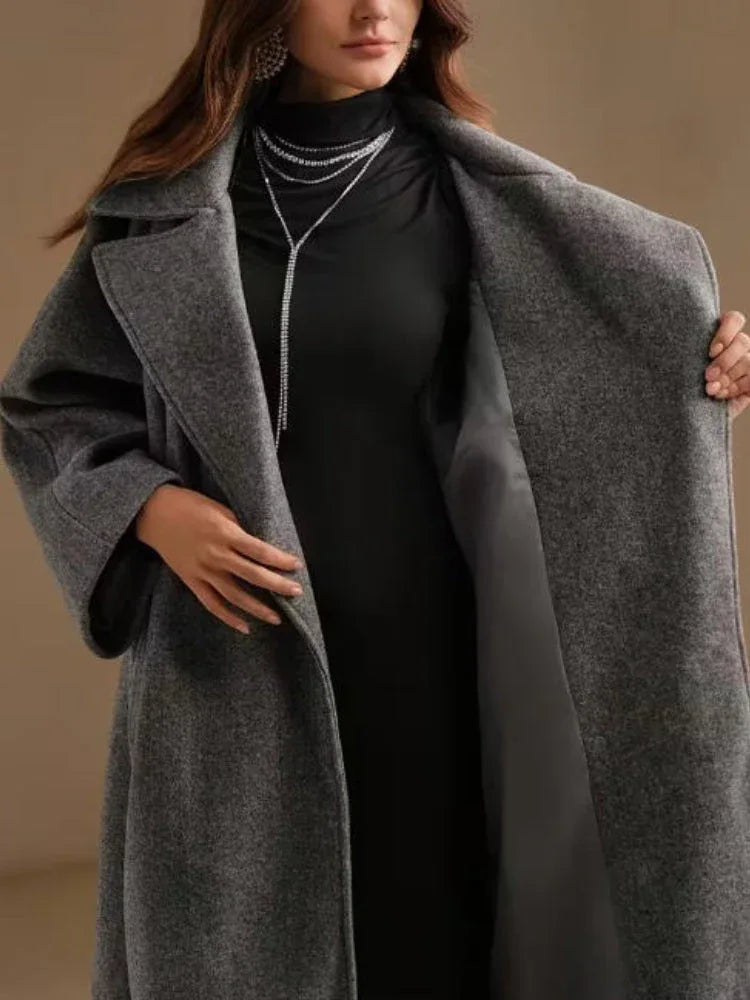 Woman opening her grey wool blend coat to reveal a black dress and silver necklace.