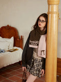 Woman in a dark jacket and plaid skirt, wearing a light pink and olive green knit scarf.