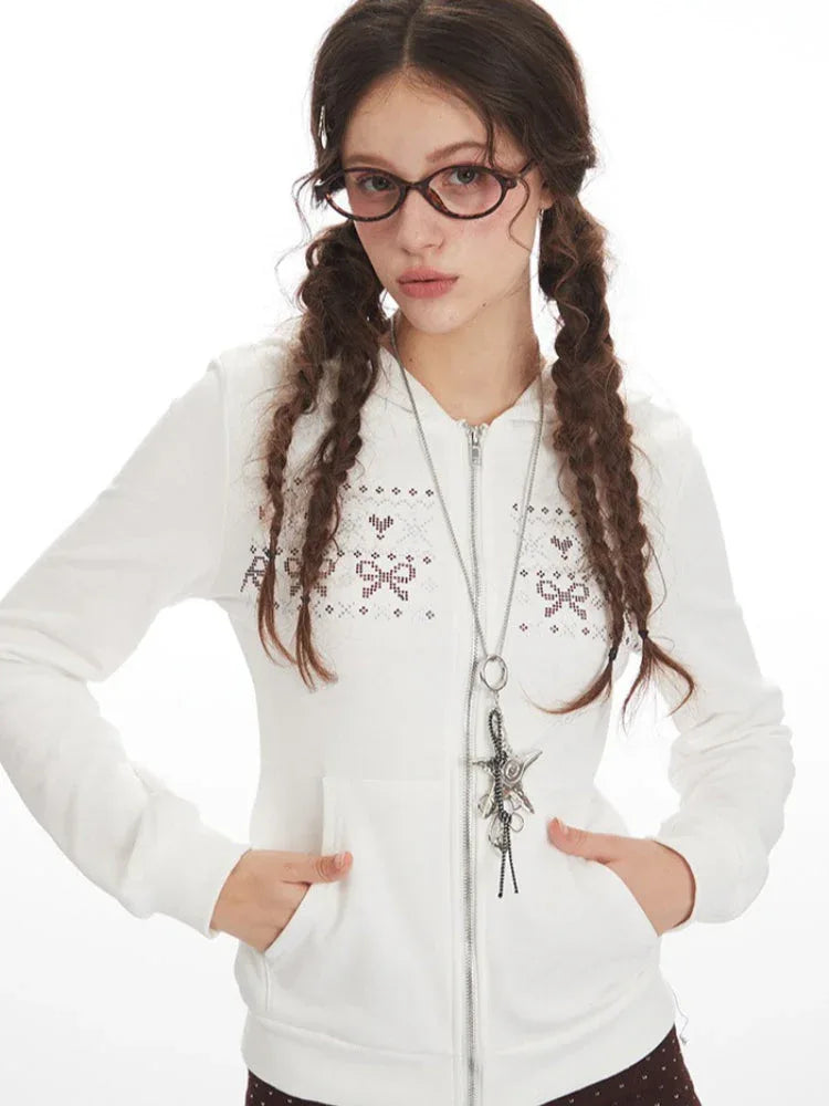 Front view of a woman's upper body wearing a white hooded zip-up jacket with a bow and heart graphic print, and a silver pendant necklace.