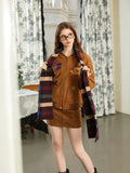 Woman holding a striped scarf in front of a brown bomber jacket and skirt