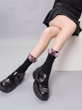 Black ribbed crew socks with pink butterfly embellishments and a ruffled cuff, paired with black platform Mary Jane shoes and a black pleated skirt.