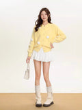 Woman wearing a yellow fuzzy knit cropped cardigan over a white top and skirt, with white socks and platform shoes.