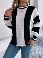 Front view of a woman with blonde hair wearing a black and white striped knit sweater and blue jeans, touching her hair.