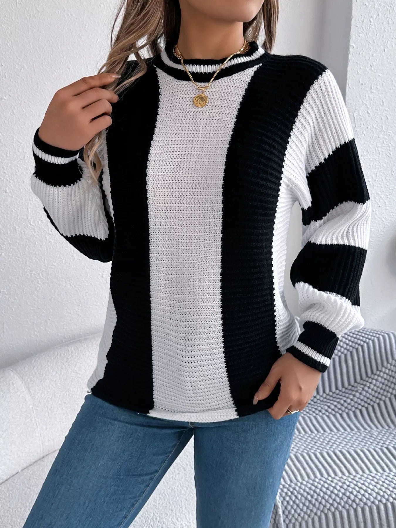 Front view of a woman with blonde hair wearing a black and white striped knit sweater and blue jeans, touching her hair.