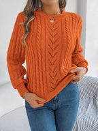 Woman wearing an orange cable knit crew neck sweater with openwork details and long sleeves.