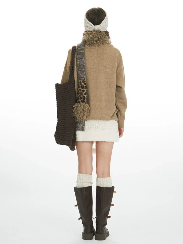 Woman wearing a tan intarsia knit sweater with birds and stars, a white textured mini skirt, white knee-high socks, and dark brown boots.