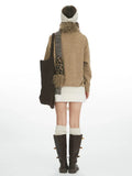 Back view of a woman wearing a tan intarsia knit sweater, white textured mini skirt, white knee-high socks, and dark brown boots, carrying a dark brown knit tote bag.