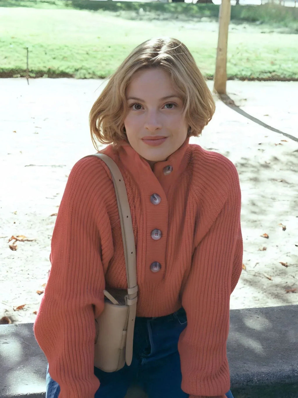 Front view of a woman wearing a coral knit sweater with a high neckline and button placket, outdoors.