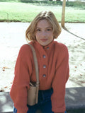 Front view of a woman wearing a coral knit sweater with a high neckline and button placket, outdoors.