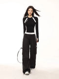 Full body shot of a model in a black and white long-sleeve athletic top and black cargo pants, holding a tennis racket.