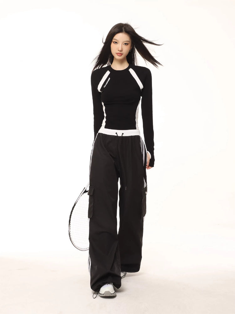 Full body shot of a model in a black and white long-sleeve athletic top and black cargo pants, holding a tennis racket.