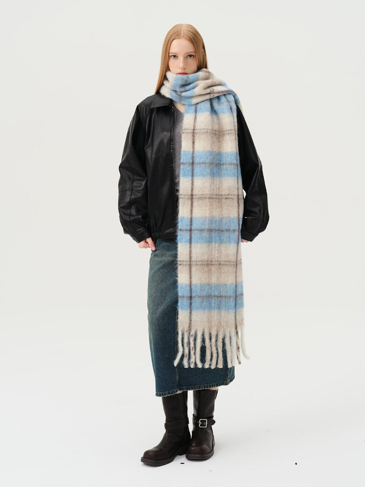 Woman wearing a plaid scarf with blue and beige squares and a fringed hem, paired with a black jacket and denim skirt.