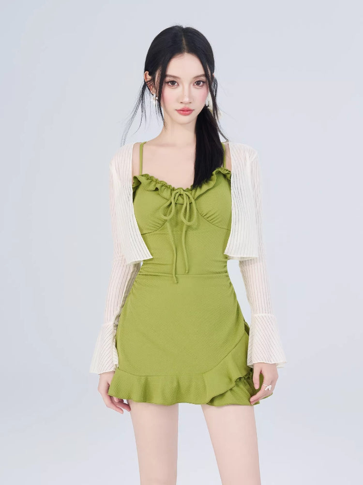 Woman wearing a green textured knit mini dress and a white open-knit cardigan with flared sleeves, styled with white lace-up sandals.