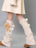Cream cable knit leg warmers with teddy bear and pom-pom details, worn with a cream dress and tan boots.