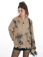 Model posing in a tan knit cardigan with abstract black print and distressed hem.