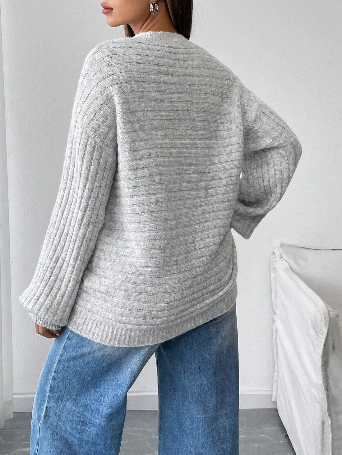 Woman wearing a light grey oversized knit sweater with long ribbed sleeves and a crew neckline, paired with blue denim jeans.