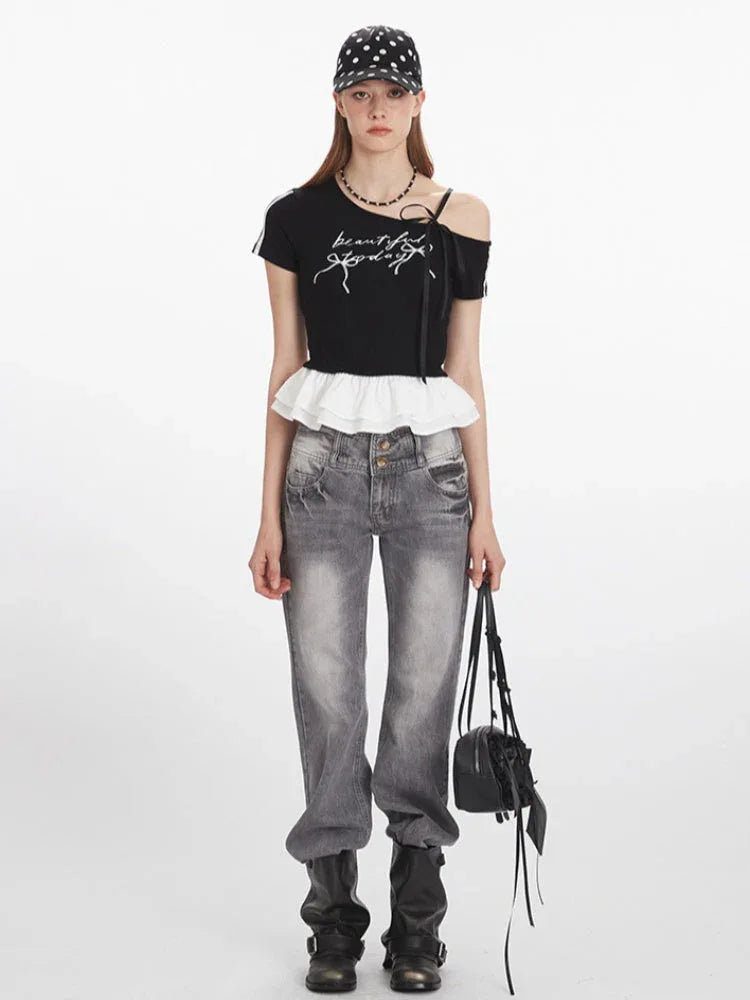 Woman wearing a black cropped t-shirt with white graphic print and ruffle trim, paired with grey jeans and a black and white polka dot cap.