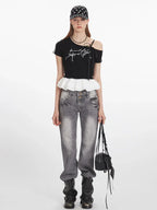 Woman wearing a black cropped t-shirt with white graphic print and ruffle trim, paired with grey jeans and a black and white polka dot cap.