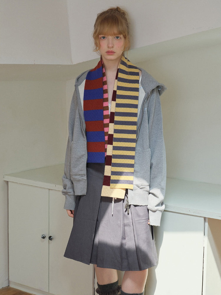 Model wearing a gray zip-up hoodie, a gray pleated skirt, and a multi-colored striped scarf.