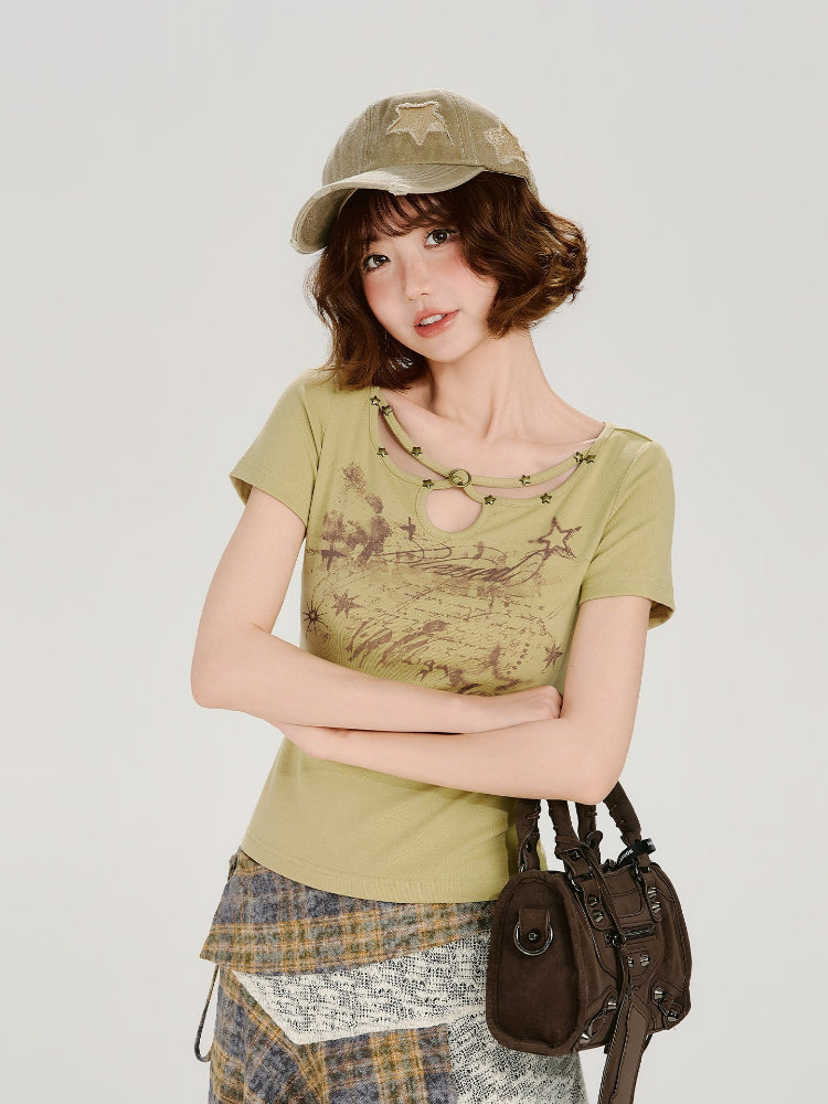 Woman posing with arms crossed, wearing the light green fitted graphic t-shirt and a plaid skirt, holding a brown handbag.