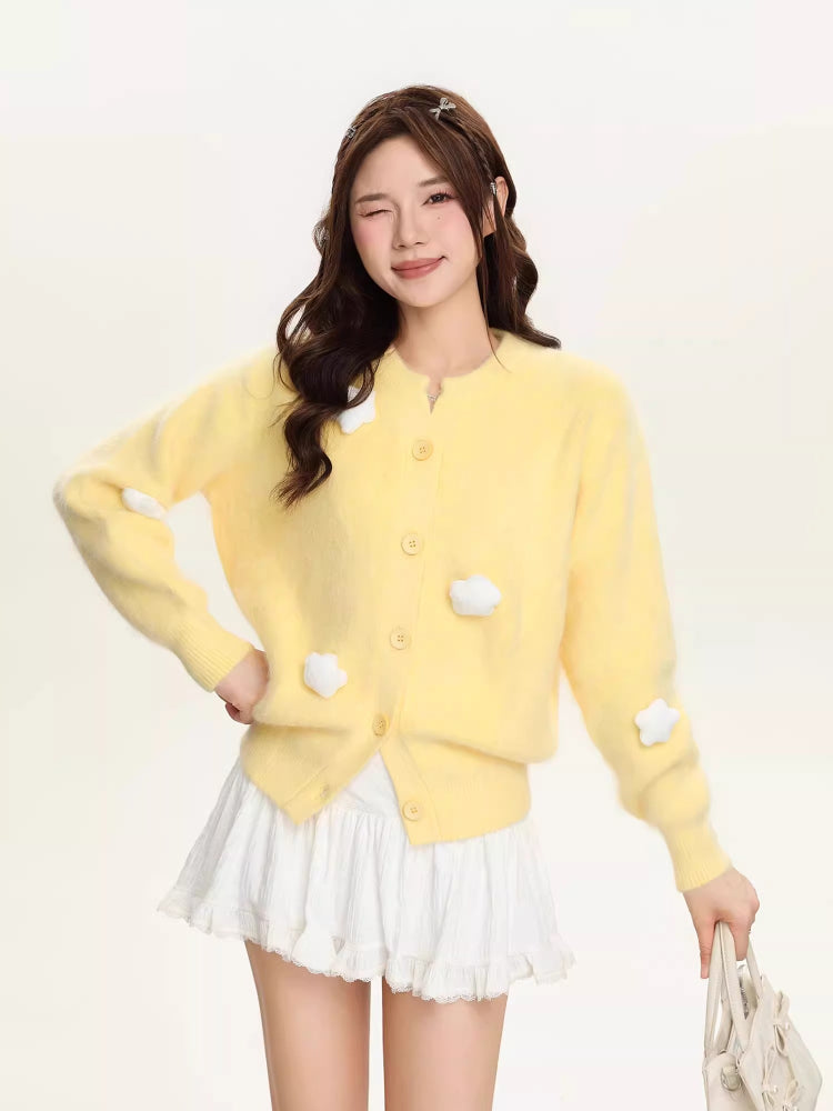 Yellow fuzzy knit cropped cardigan with white cloud embellishments and button front closure, worn by a woman with long brown hair.