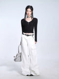 Woman wearing a black long-sleeve ribbed knit top and white cargo pants, accessorized with a belt and holding a silver handbag.