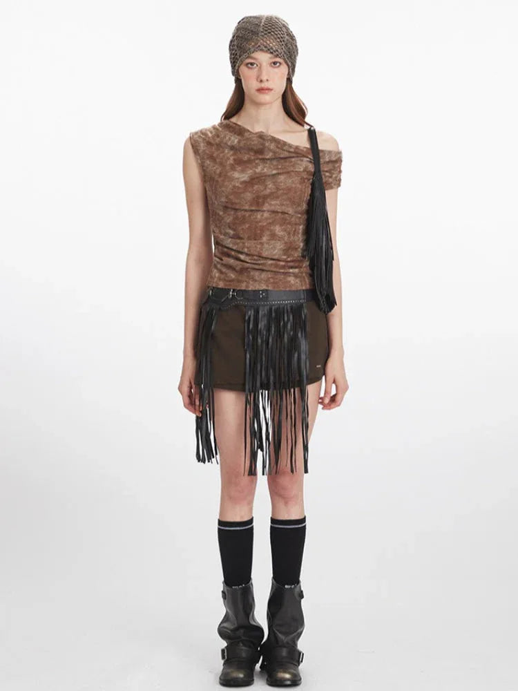 Model wearing a brown textured knit top with an asymmetrical neckline and draping, paired with a dark skirt with fringe detail.