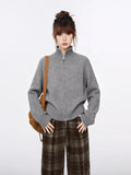 Front view of a woman in a grey zip-up turtleneck sweater and plaid trousers