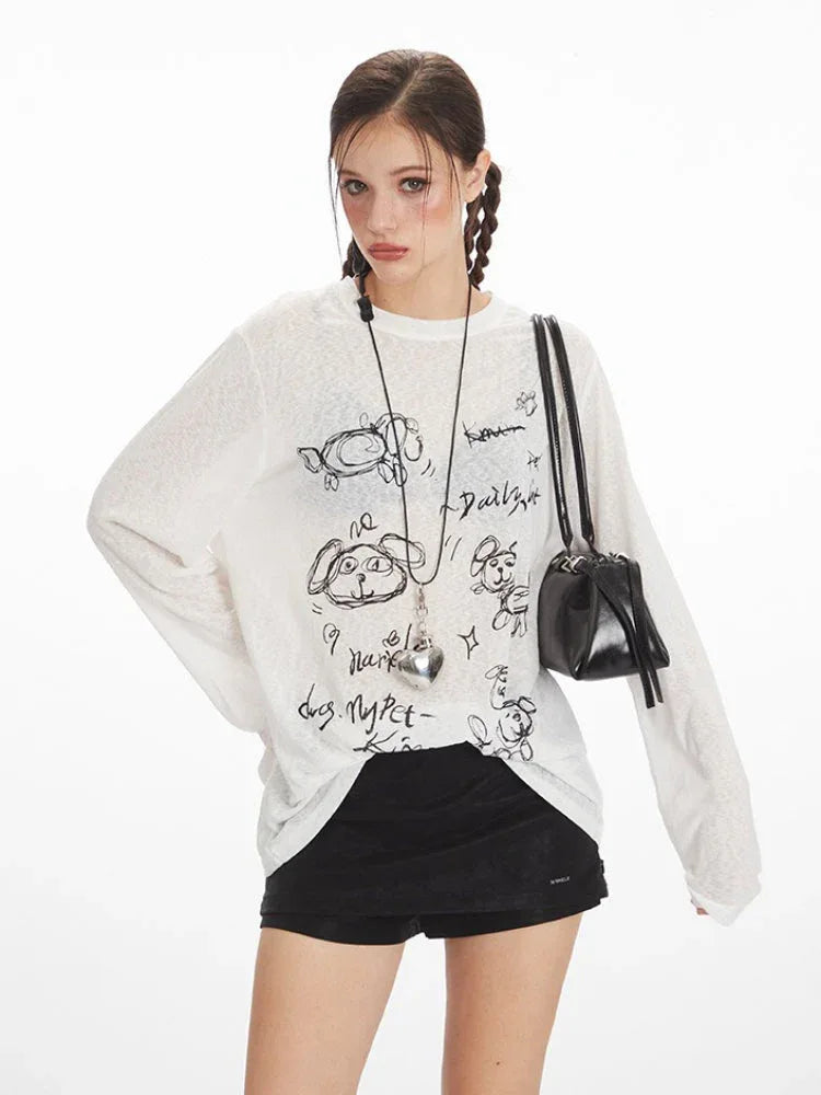 Close-up of a woman wearing a white long-sleeve sheer knit t-shirt with a black dog graphic print and text, and a silver heart pendant necklace.