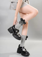 A person wearing gray crew socks with a gray flower embellishment and bow detail, demonstrating the socks with platform Mary Jane shoes.