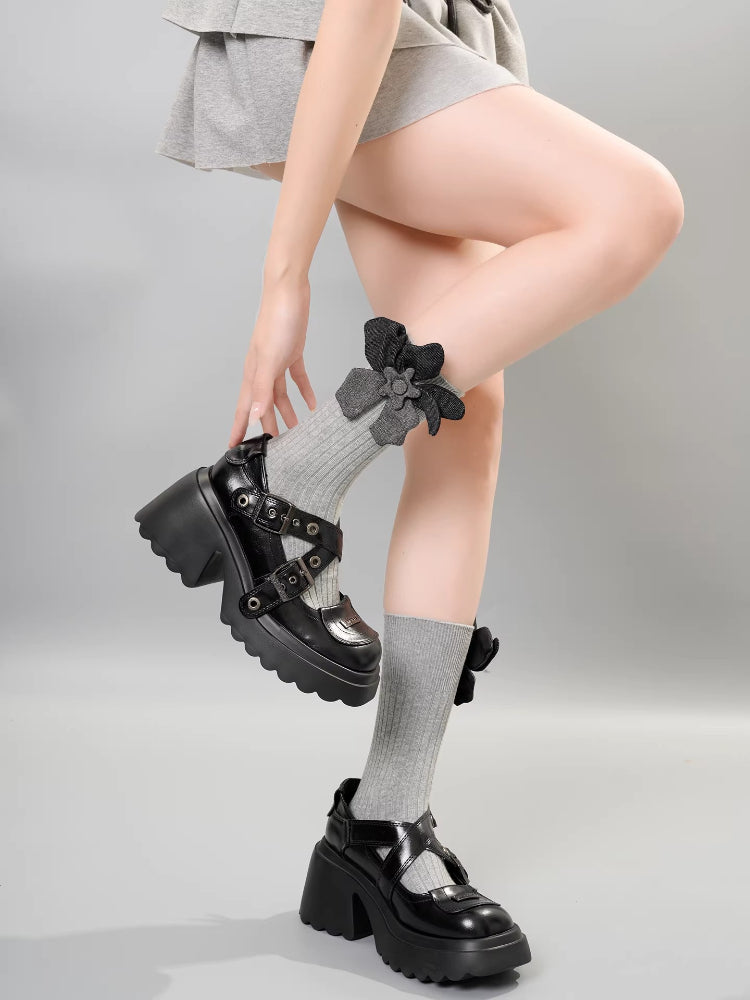 A person wearing gray crew socks with a gray flower embellishment and bow detail, demonstrating the socks with platform Mary Jane shoes.