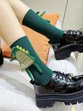 Green ribbed mid-calf socks with a 3D dinosaur applique on the ankle, paired with black platform shoes.