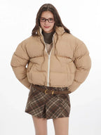 Front view of a woman wearing a beige cropped puffer jacket with a white zipper.